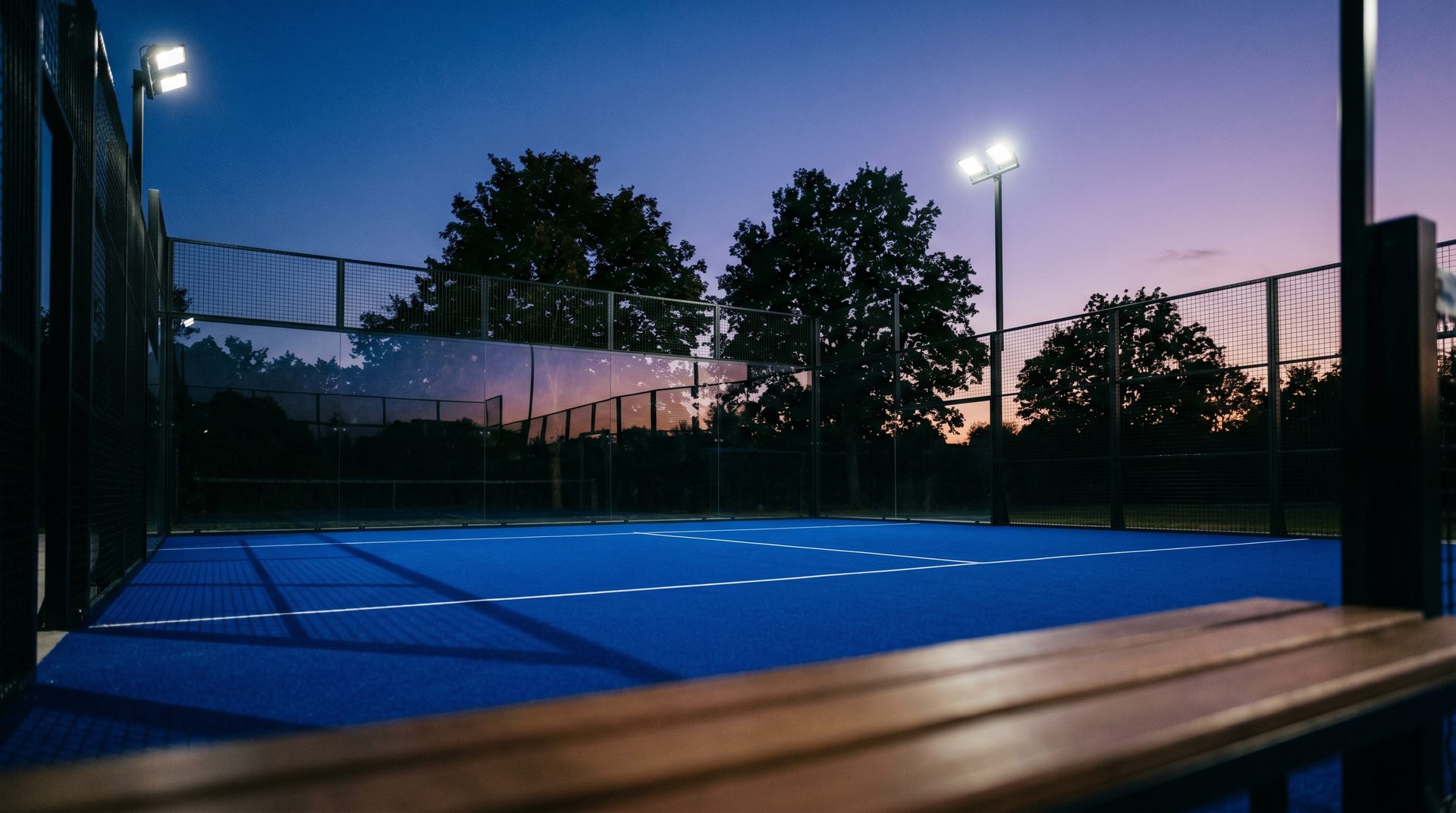 Padel Court bei Dämmerung mit Flutlicht und Bäumen am Rand